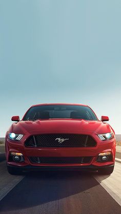 the front end of a red ford mustang on a road with blue sky in the background