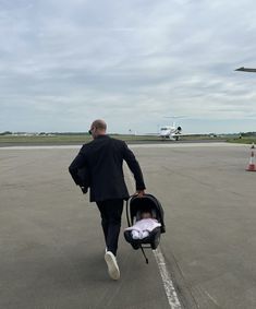 a man walking across an airport tarmac with a baby in a stroller