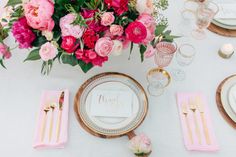 a table setting with pink flowers and goldware