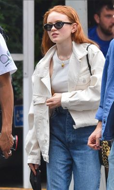 a woman with red hair wearing sunglasses and a white jacket is walking down the street