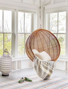 a hanging chair in front of a window with shoes on the floor next to it