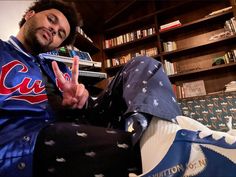 a man sitting on top of a couch in front of a bookshelf making the peace sign