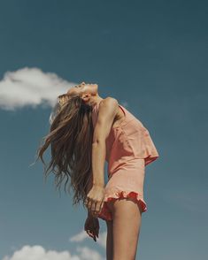 a woman standing on top of a sandy beach next to a blue sky with clouds