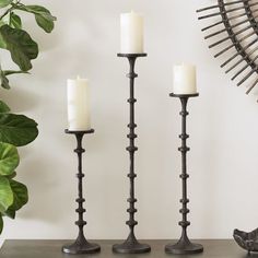 three candles are sitting on a table next to a potted plant and wall decoration