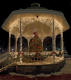 a gazebo covered in christmas lights with a tree on the top and decorations around it