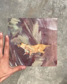 a hand holding up a piece of art with a dog on it