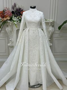 a white wedding gown with long sleeves and a high neckline, on display in front of