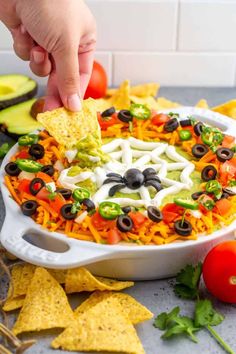 a hand dipping a tortilla chip into a white bowl filled with mexican salad