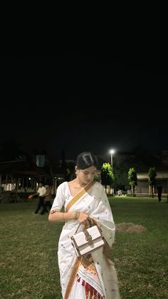 a woman in a white sari is standing on the grass with her handbag