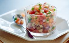 a small glass bowl filled with chopped vegetables on top of a white plate next to a spoon