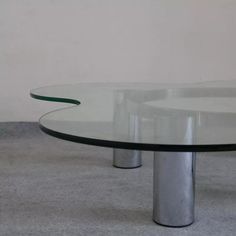 an oval glass table with metal legs on carpeted floor in front of white wall