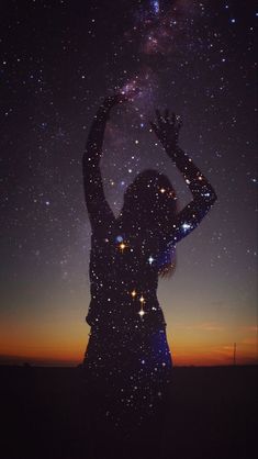 the silhouette of a woman with her hands up in the air, against a night sky filled with stars