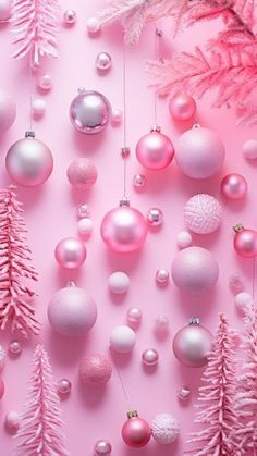 pink and white christmas ornaments hanging from strings on a pink background with fir trees in the foreground