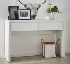 a cow head is on the wall above a white table with a basket and framed pictures