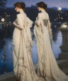 two women in white dresses standing next to each other on a ledge near water and flowers