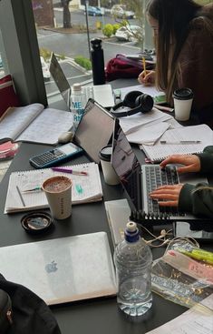 two people sitting at a table with laptops and notebooks on top of them