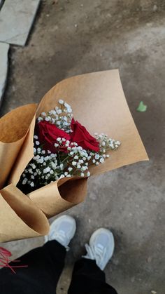 a person holding a bouquet of flowers in their hand on the ground next to someone's feet