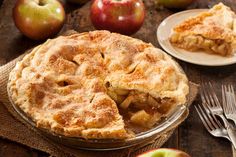 an apple pie on a wooden table with two plates and forks