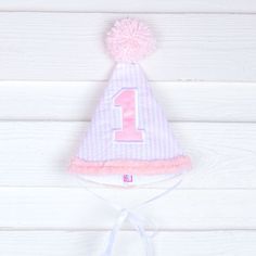 Happy 1st birthday to your little one! This cone hat with a pom pom on top is perfect for cake smashing pictures and first birthday celebrations. Your little one will look so adorable in this darling hat styled to match their big day! Fun Birthday Party Hat Supplies, Playful Mini Hats For Birthday, Cute Adjustable Hat For First Birthday, Cute Pink First Birthday Party Supplies, Playful Adjustable Mini Hats For Birthday, Playful White Party Supplies For First Birthday, Cute White Hat For First Birthday, Cute Pink Mini Hat For First Birthday, Playful Adjustable Hats For Birthday