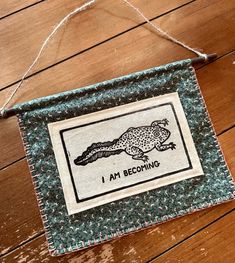 a sign hanging on the side of a wooden floor that says i am becoming with an alligator