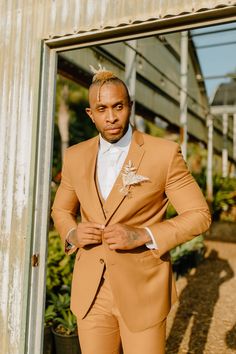 a man wearing a tan suit and white shirt standing in front of a metal building