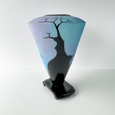 a black and blue vase with a tree painted on the front, sitting on a white surface