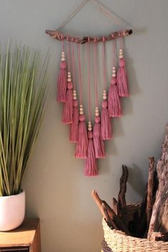 a pink wall hanging with tassels on it next to a potted plant