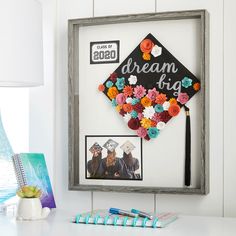 a graduation cap made out of paper flowers is displayed on a white desk next to a framed photo