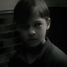 a young boy is staring at the camera in a dark room with black tiles on the walls