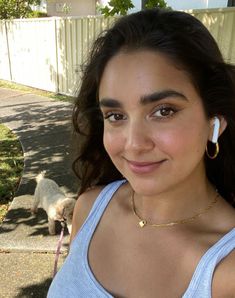 a woman with ear buds on her ears smiling at the camera while standing in front of a house