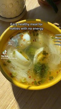 a yellow bowl filled with soup and broccoli on top of a wooden table