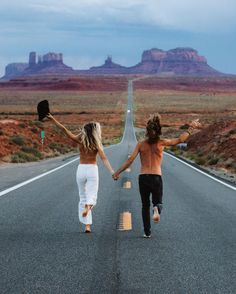 two people holding hands while walking down an empty road