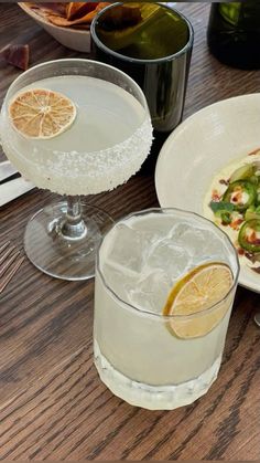 two glasses filled with drinks sitting on top of a table next to plates and utensils