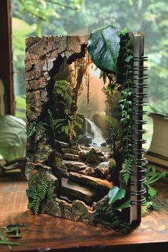 an open notebook with a waterfall in the middle and green plants growing out of it