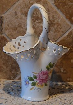 a white vase with pink flowers on it sitting on a table next to a tile wall