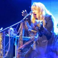 the woman is singing on stage with her guitar and other musicians in the back ground