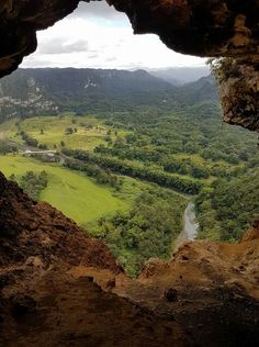 the view from inside a cave looking down at a valley and river in the distance