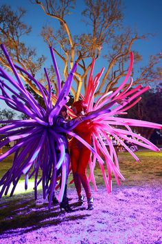 two people are standing in the grass with purple and red decorations on their arms,