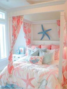 a white bed topped with pink and blue pillows next to a starfish wall hanging