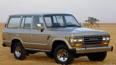 an suv is parked in the middle of a field with some animals grazing behind it