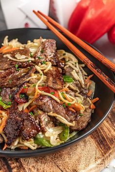 a black plate topped with beef and noodles next to chopsticks on a wooden table