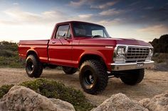 a red pickup truck parked on top of a dirt road next to rocks and bushes