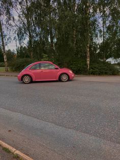 a red car is parked on the side of the road in front of some trees