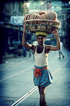 a man walking down the street carrying a basket on his head with food in it