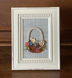 a white frame holding a small basket with flowers on the front and bottom, hanging on a wooden wall