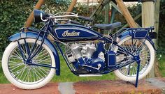 an old fashioned blue motorcycle parked on top of a stone slab in front of a wooden structure