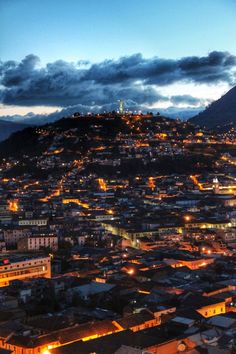 an aerial view of a city at night with lights on the buildings and mountains in the background