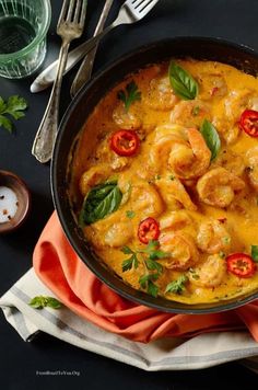 a skillet filled with shrimp and tomatoes on top of a table next to silverware