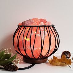 a table topped with a vase filled with lots of pink stones next to leaves and pine cones