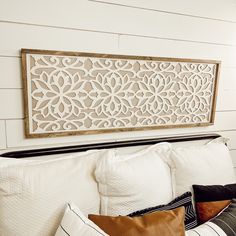 a white bed with pillows and a decorative wall hanging above it's headboard